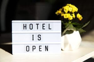 Signboard displaying 'Hotel is Open' next to a vase with yellow flowers, symbolizing local SEO for hotels and improved visibility.